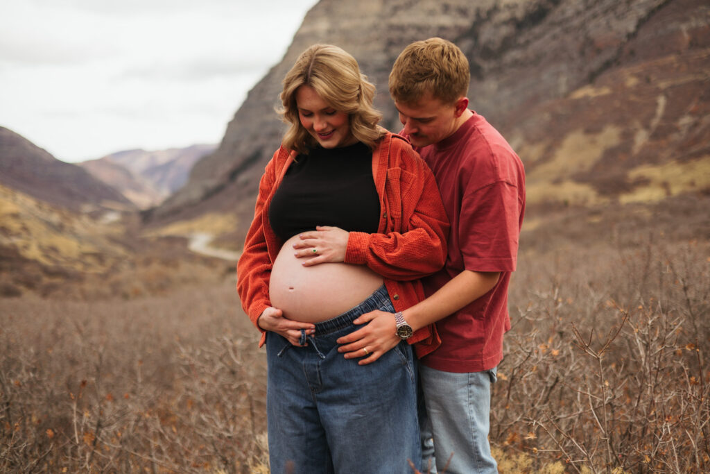 pregnant woman hugged by husband both looking down at baby bump