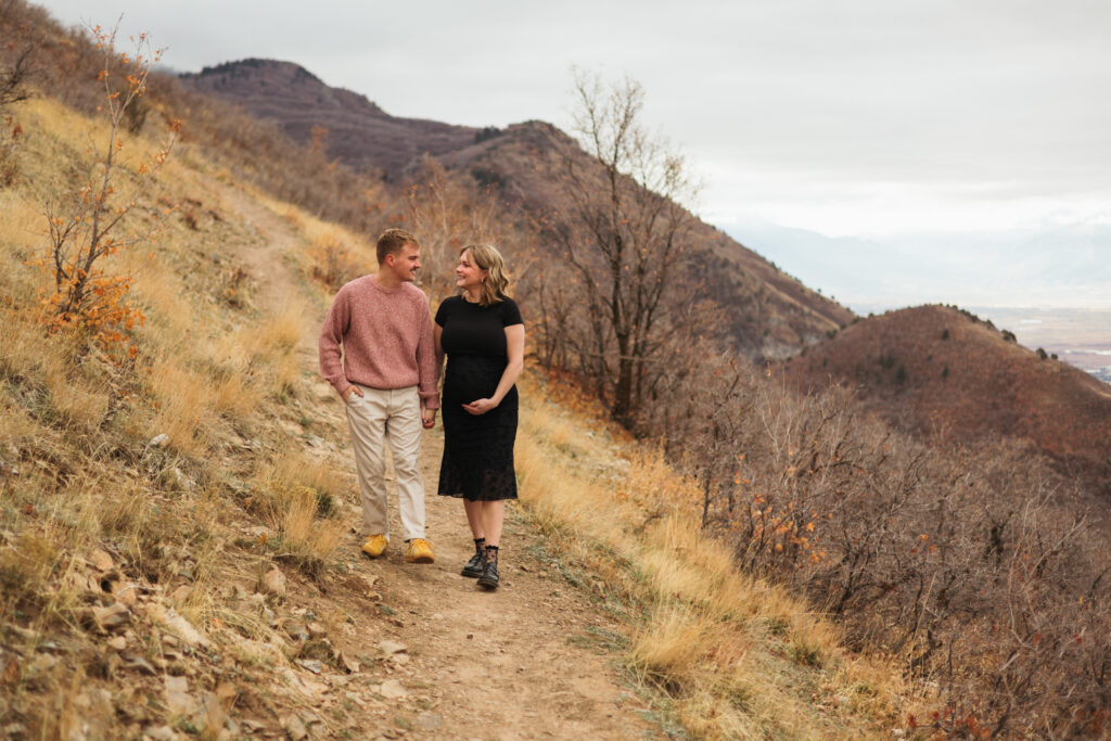 pregnant woman holding hands with husband walking on trail smiling at each other