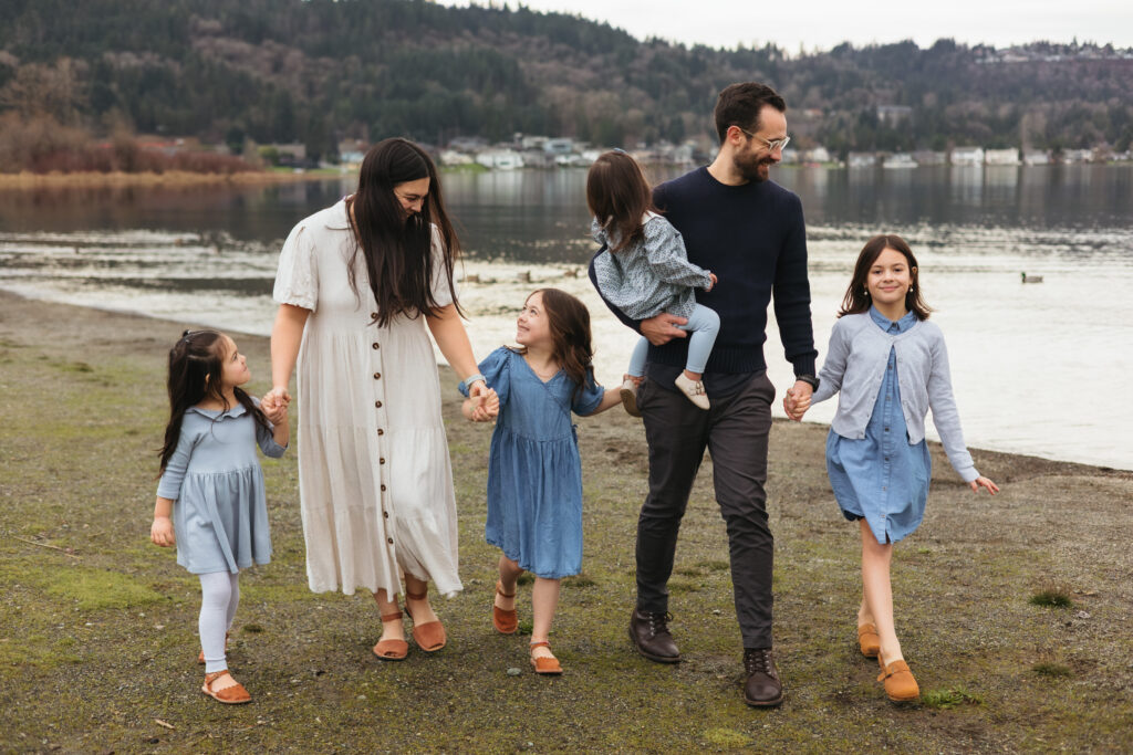 Family in blue scheme holding hands walking towards camera Sammamish lake