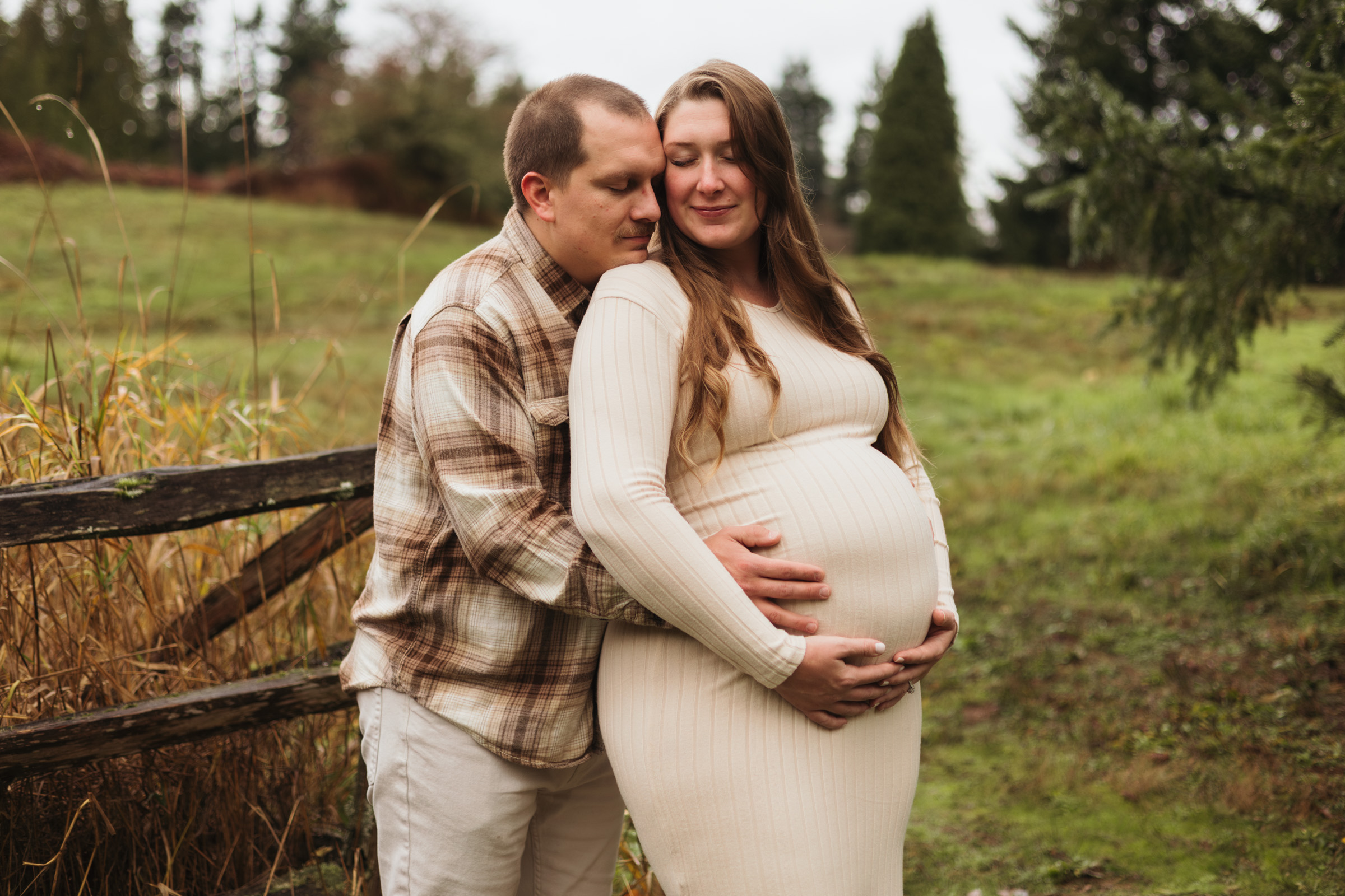 Maternity photo of women in white dress with husband hugging in Seattle area field