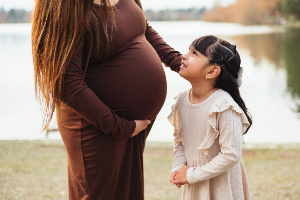 sweet moment between pregnant mother and daughter looking at each other at Seattle lake