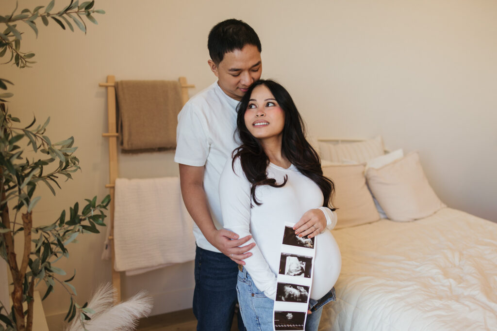 pregnant woman holding ultrasound while being hugged by husband in cozy bellevue home
