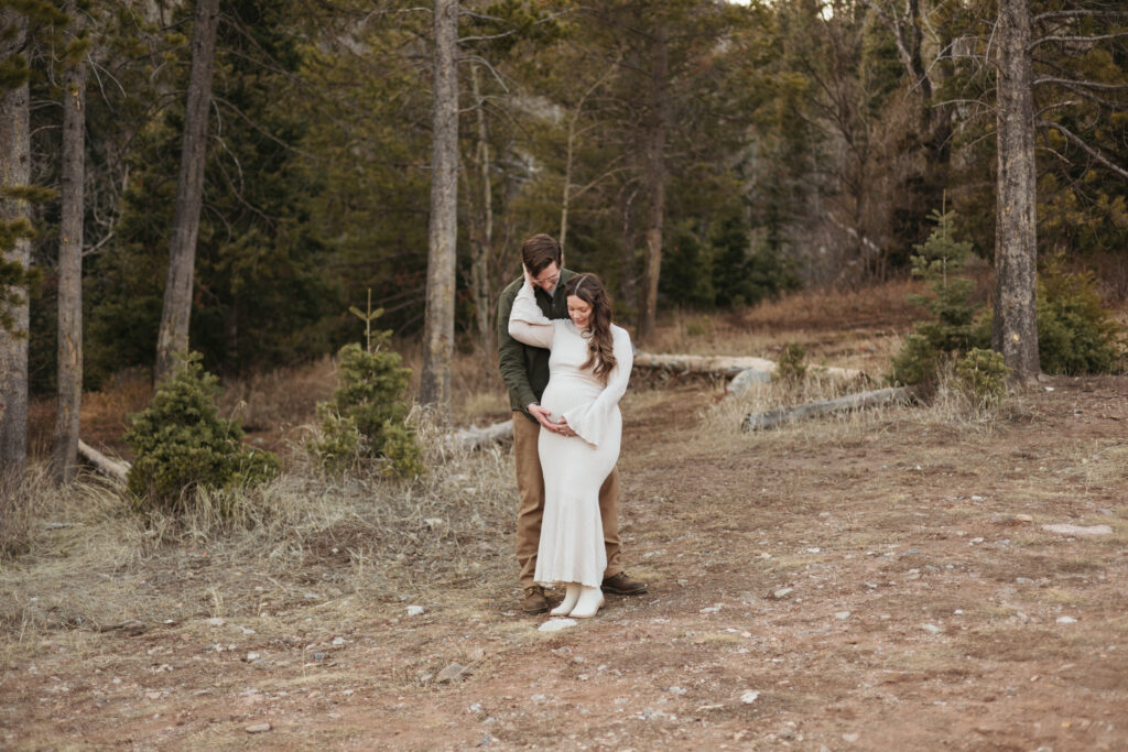 beautiful outdoor maternity session woman in white flowy dress hugged by husband