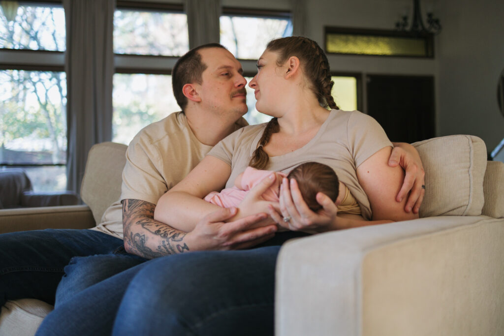 mother breastfeeding newborn baby looking at husband hugging her in bellevue home