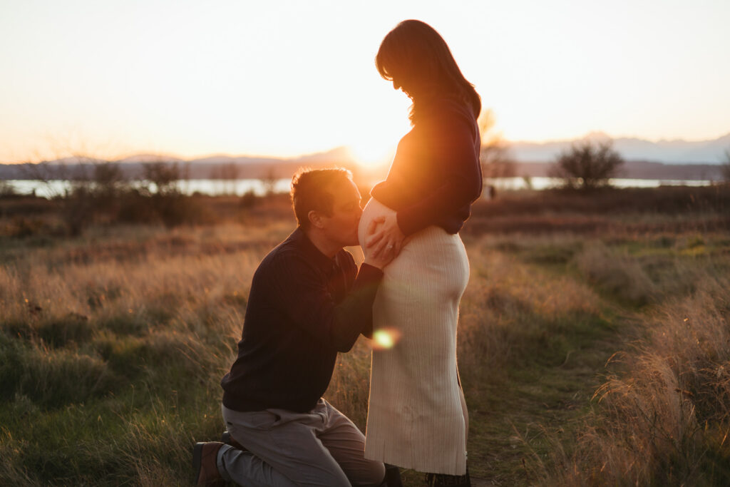 Seattle couple husband on kneels kissing pregnant belly Discovery Park