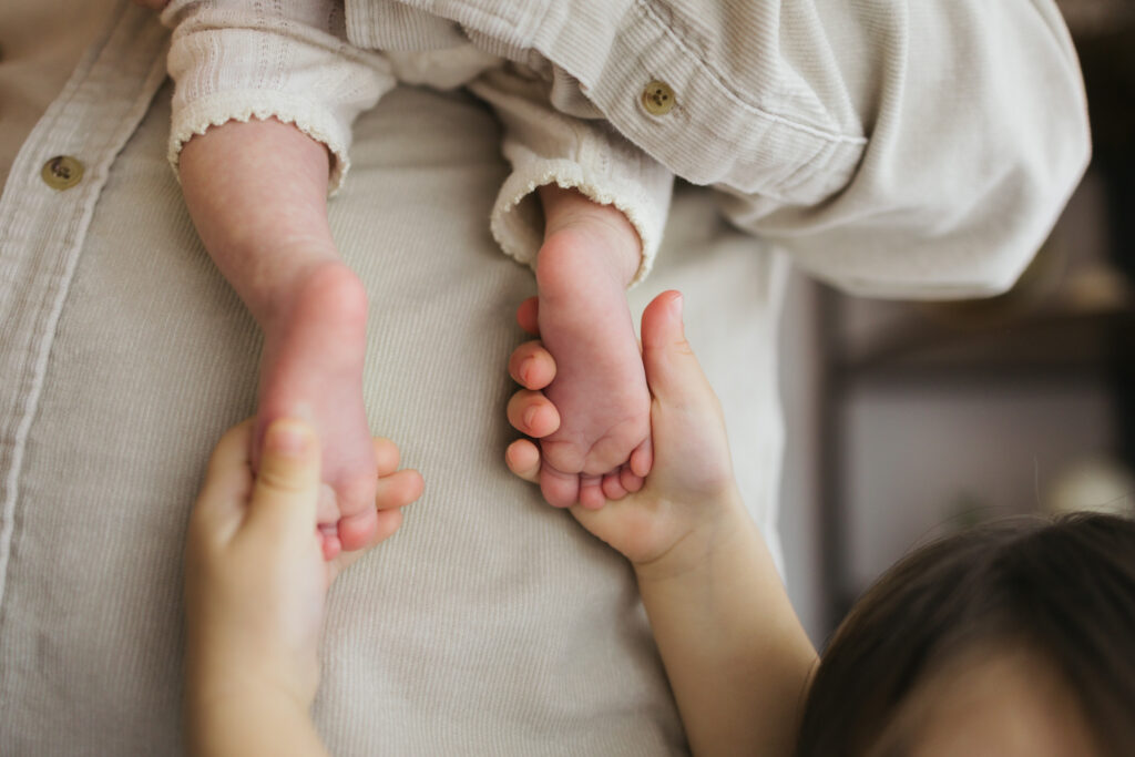 toddler holding newborn's feet in cream colored clothes Seattle home 