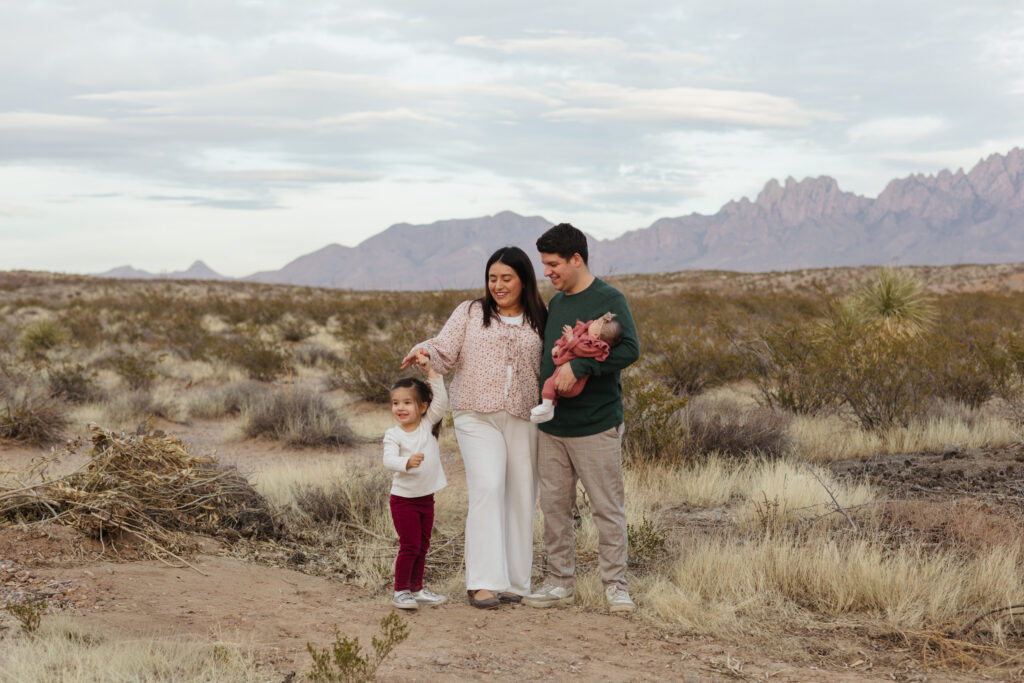 family of four wearing pink and green scheme, hugging while toddler dances.