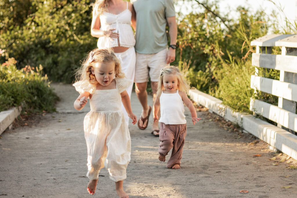 sisters running in front of mom and dad towards the camera on the beach
