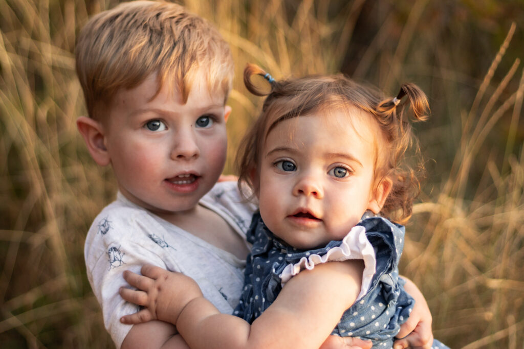 Brother and sister toddlers hugging each other looking at the camera at sunset